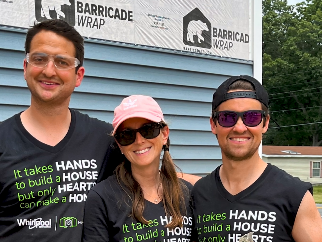 Three volunteers posed in front of a house under construction.