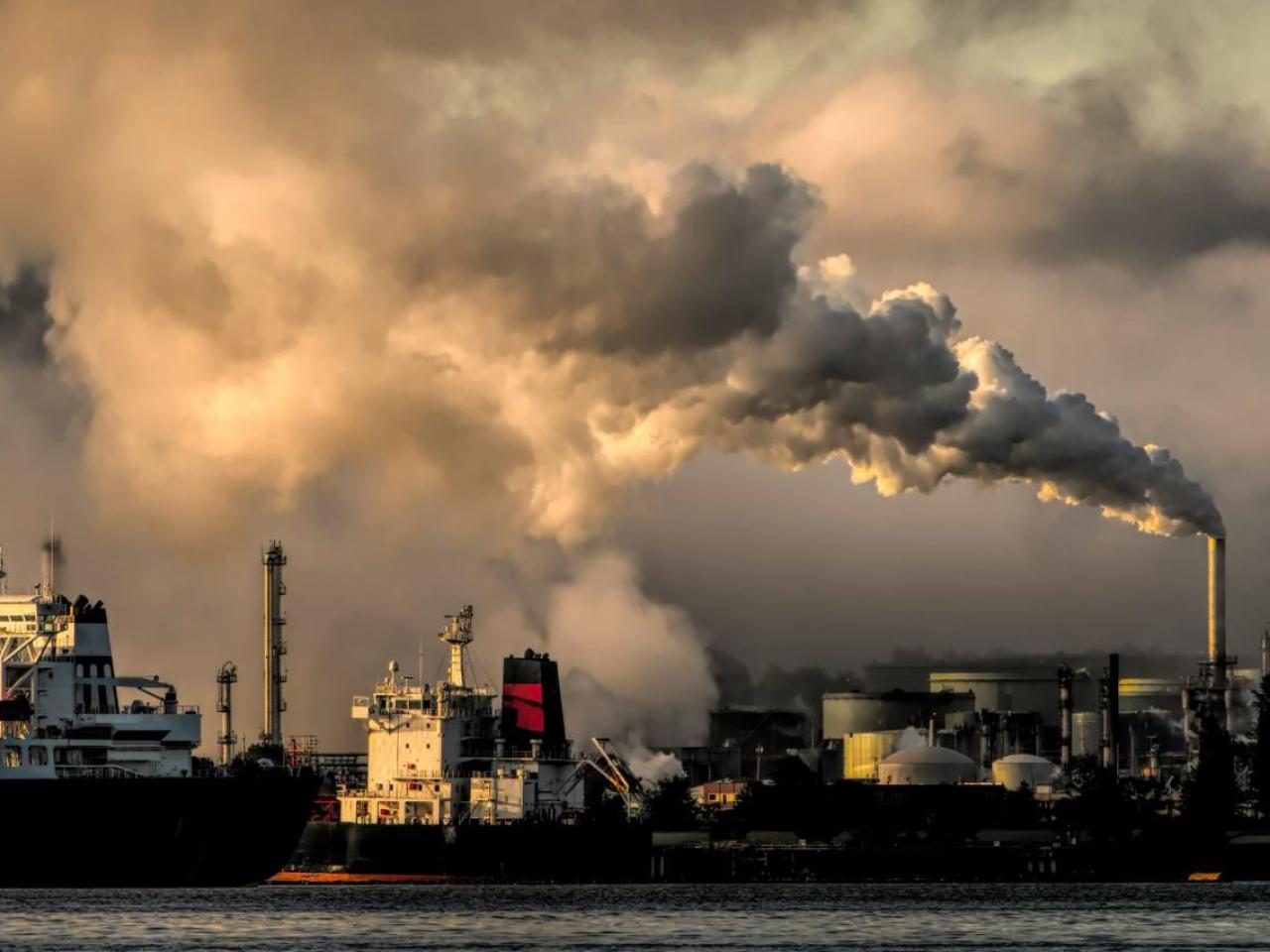 Smoke stacks with billowing clouds and a cloud covered sky behind.