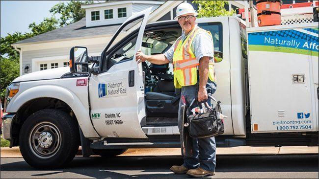 A utility worker standing with a hand on an open door to a utility truck in a residential area.