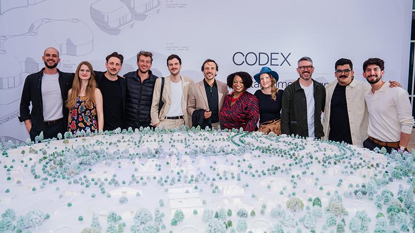 Group of 11 women and men stand behind a model of 3D-printed homes