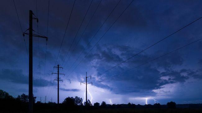 Power lines in the dark, lit by striking lightning in the distance.