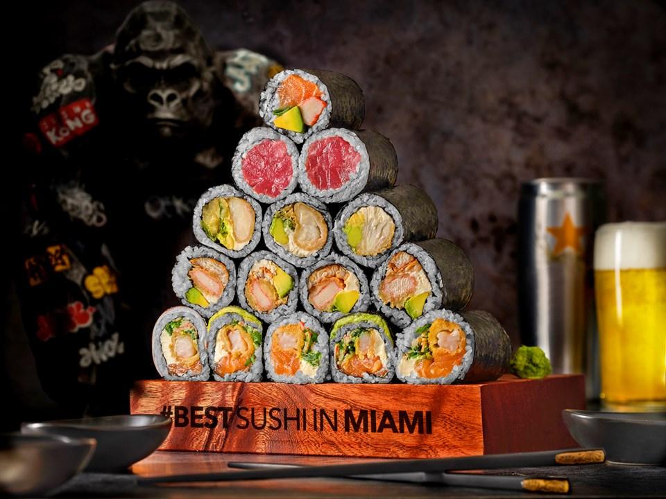 A pyramid of sushi rolls in a tray, beverages behind them.