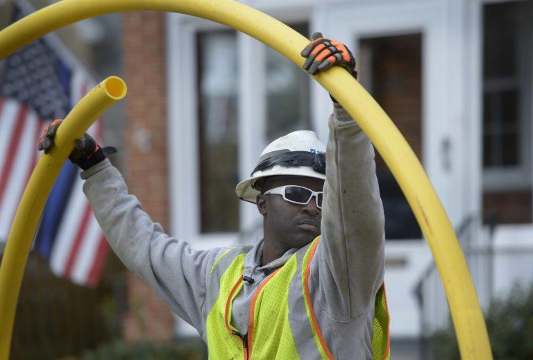 A utility worker holding up a yellow tube outside.