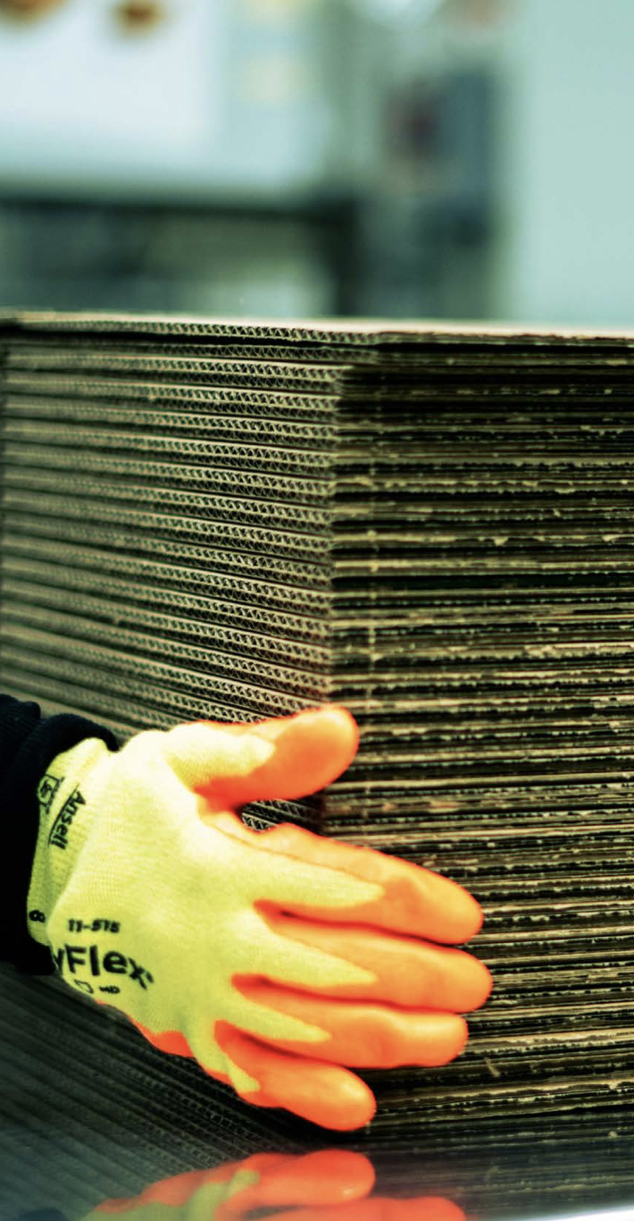 hand in an orange and yellow glove holding a stack of cardboard