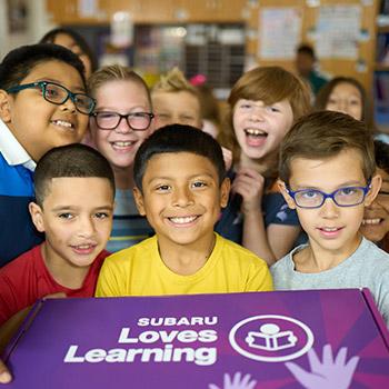 a group of school children holding a purple Subaru Loves Learning® box