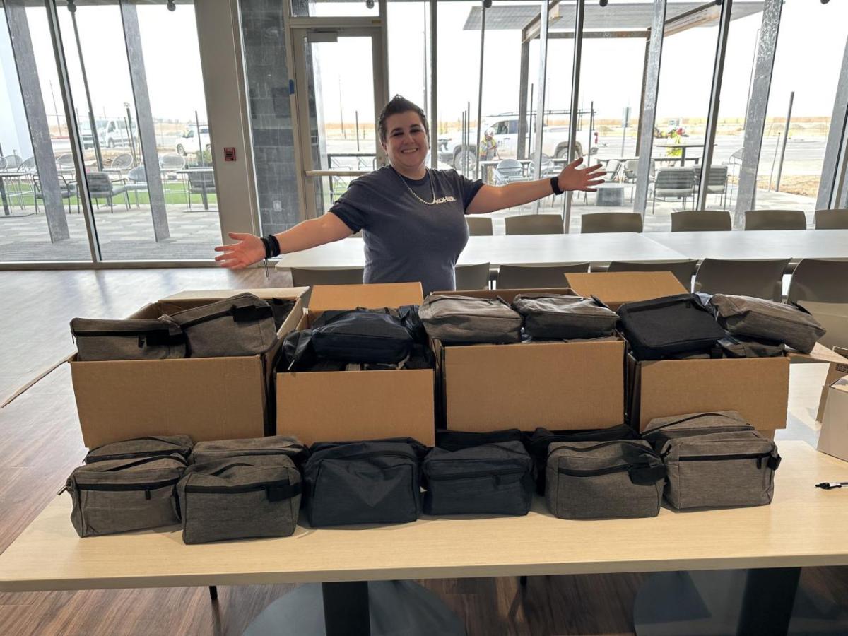 volunteer standing behind a table full of square gray zippered bags