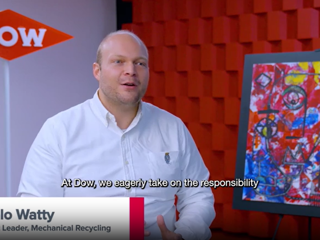 Juan Pablo Watty, seated for an interview. A White wall with Dow logo behind them, a red textured wall and painting on the right.