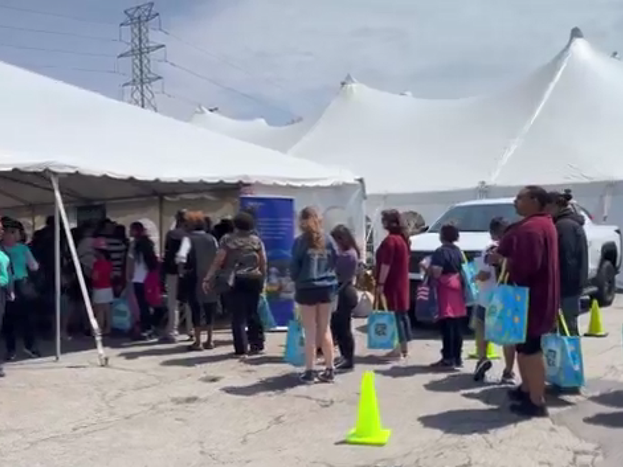 A line of people going under a large white tent. Volunteers standing to the side.