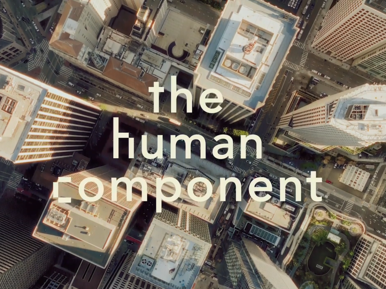 "the human component" over an aerial view of tall city buildings.