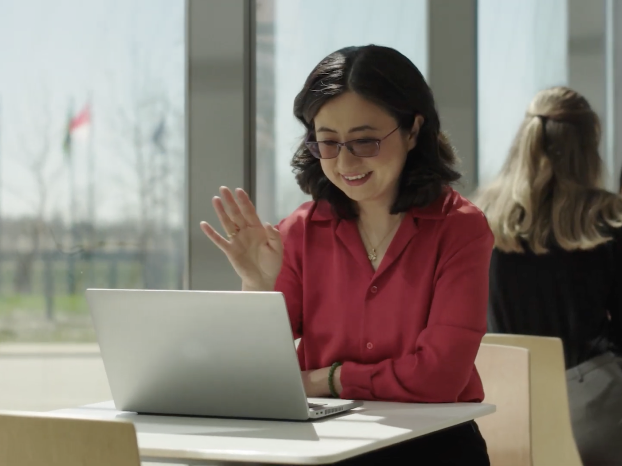 A person sat at a table waving at their laptop