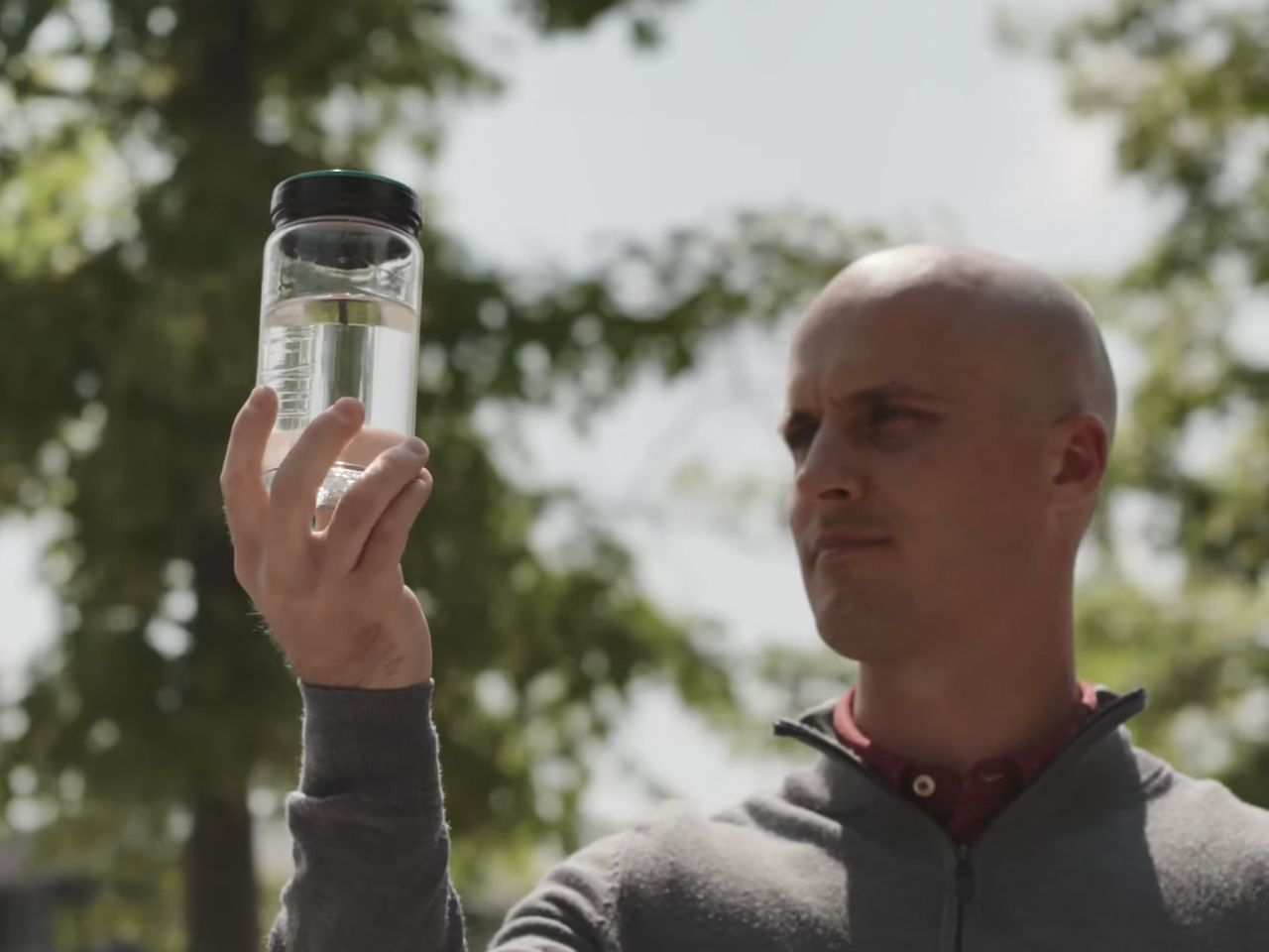 A person holding up a clear bottle of fluid outside.