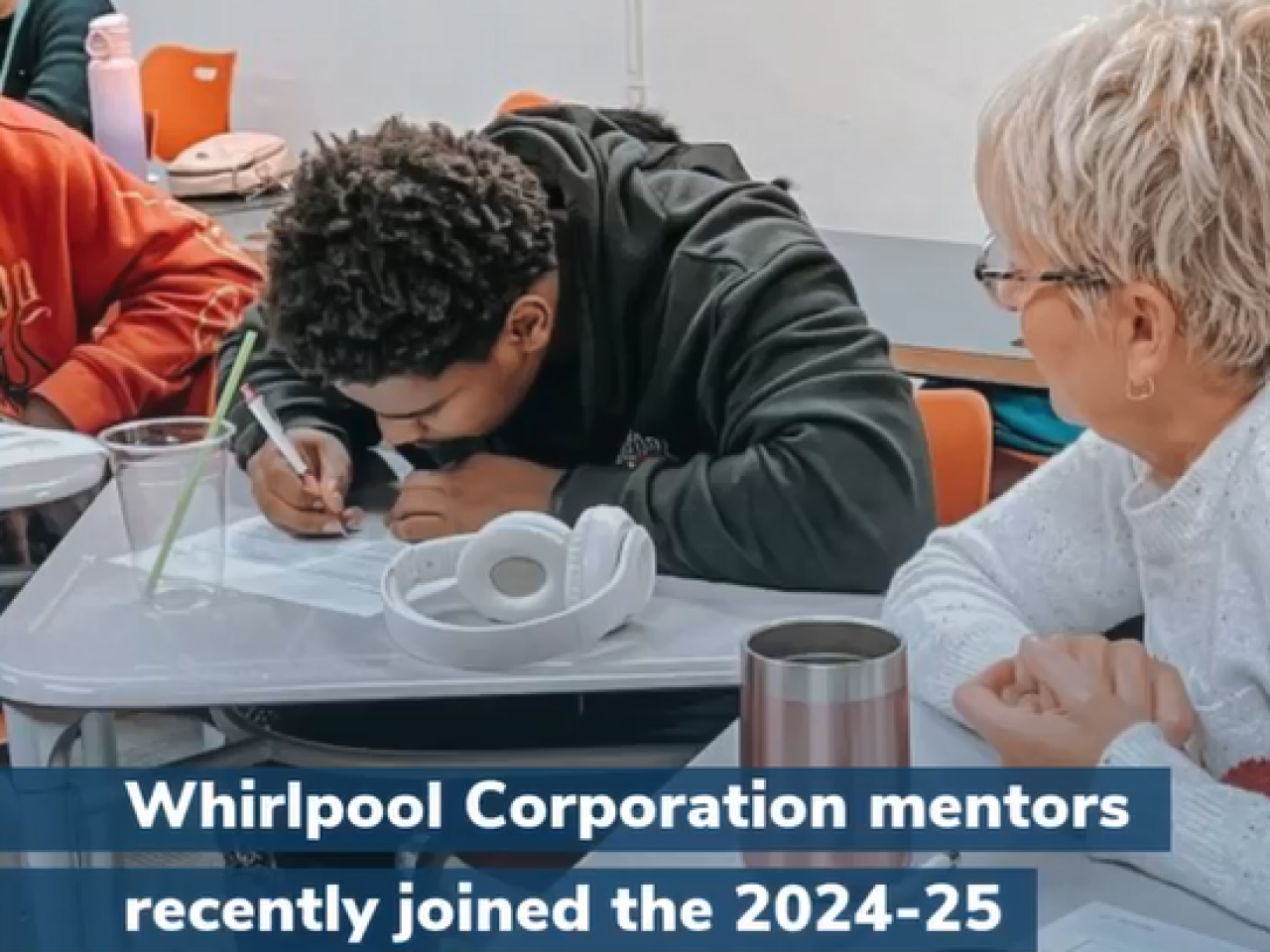 A mentor watching as a student writes at a desk.