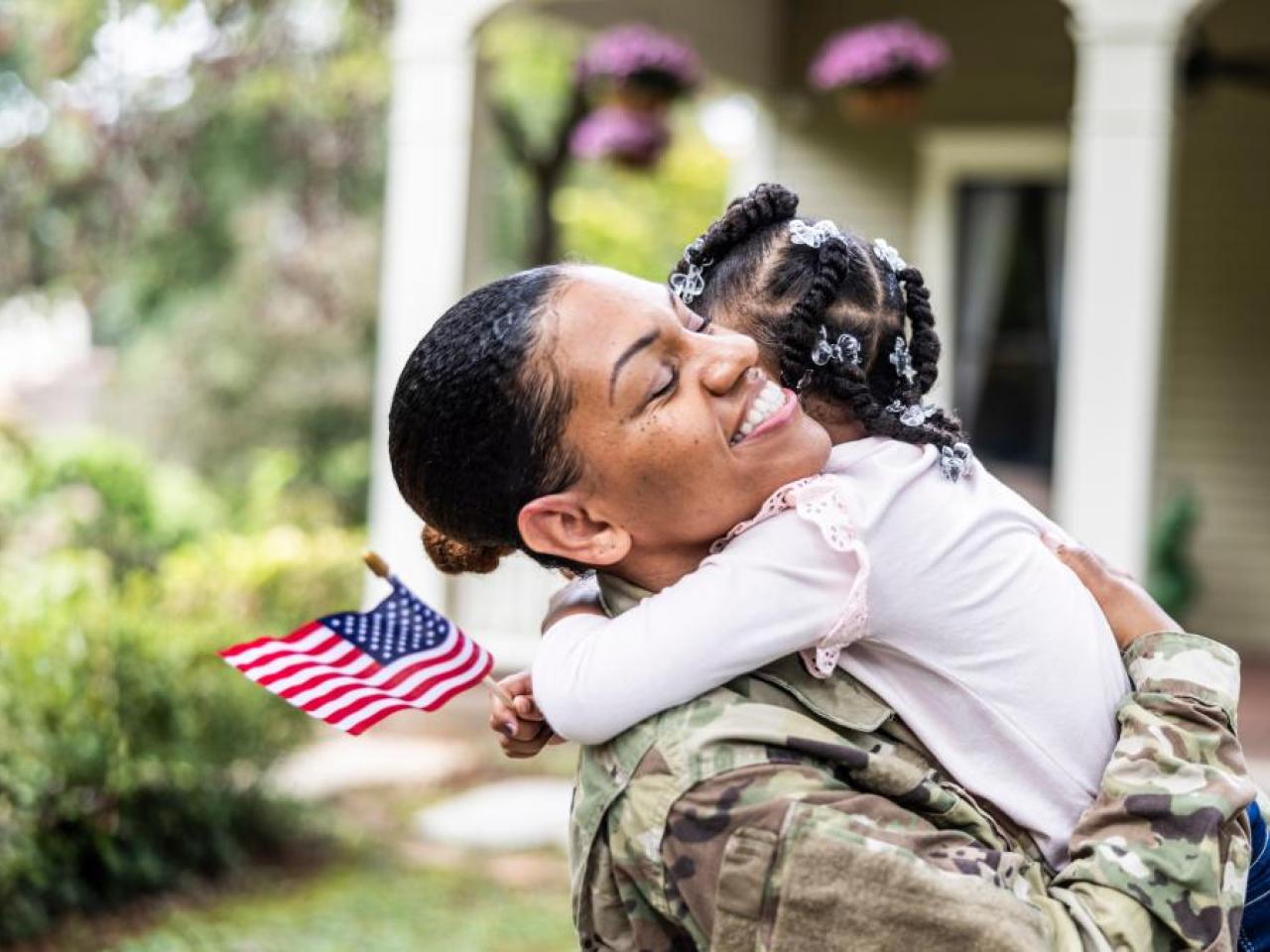 A veteran hugging a young child who is holding a small American flag