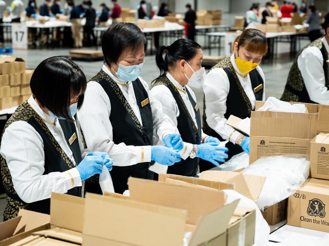 People in masks and gloves working with boxes on tables
