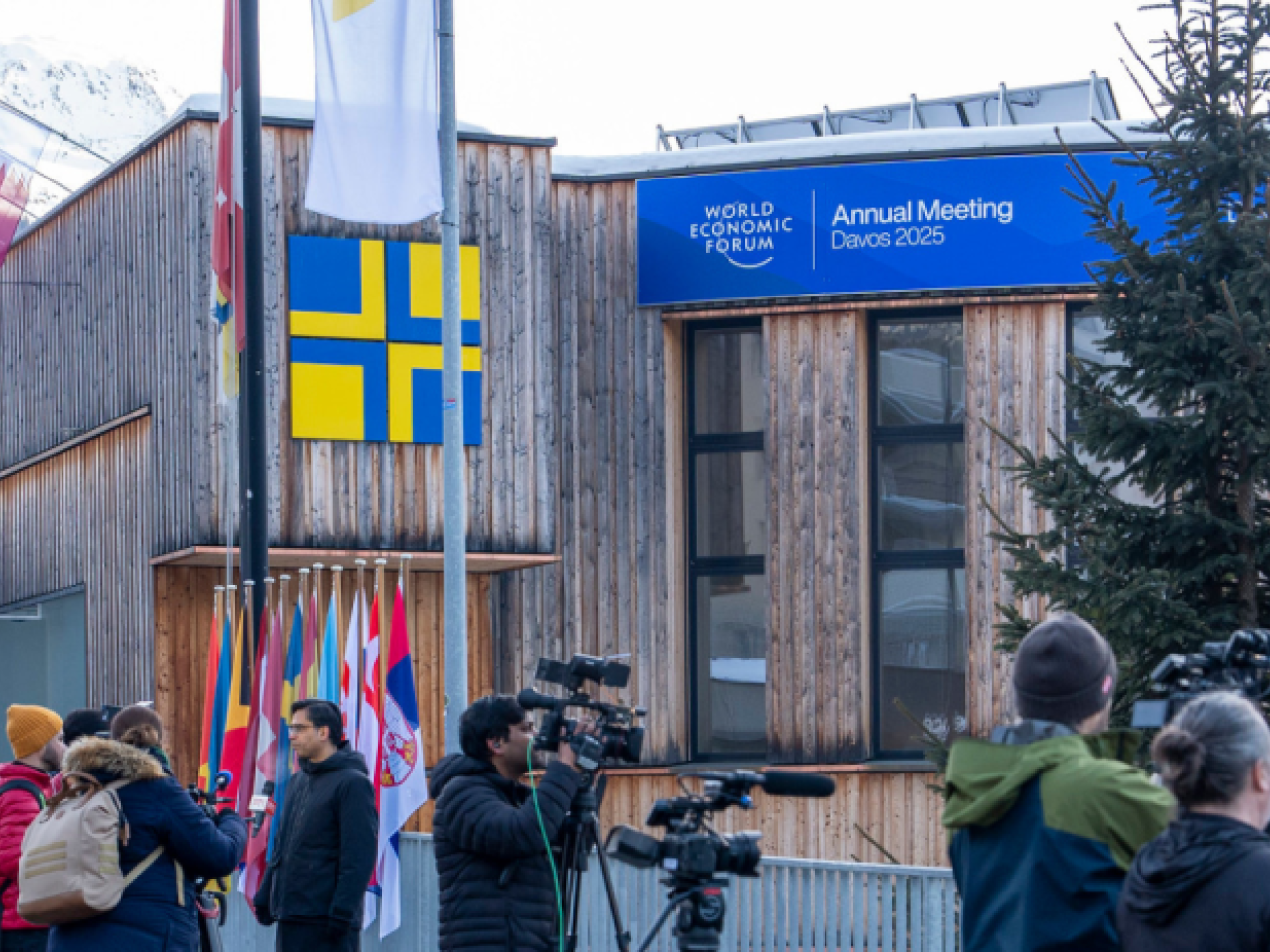 A building with Alps in the background, and people gathering outside