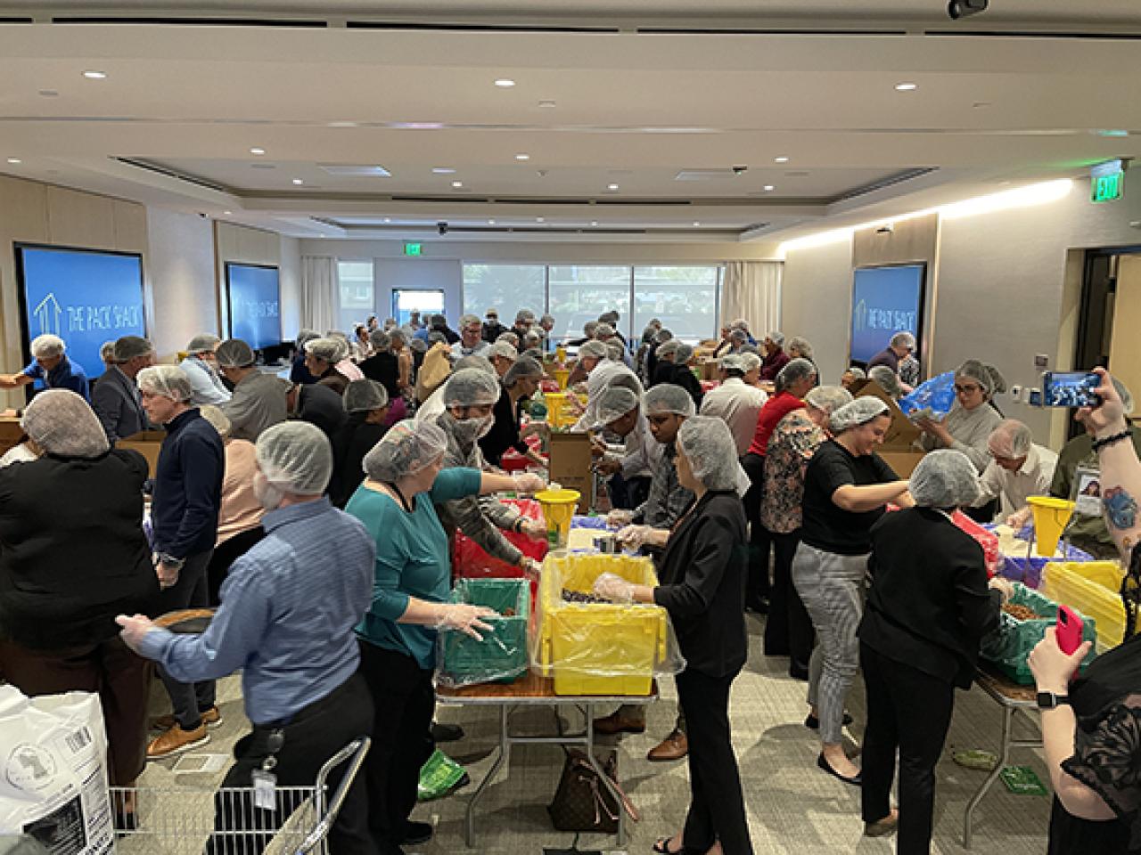 A room full of people in hair nets packing boxes on tables