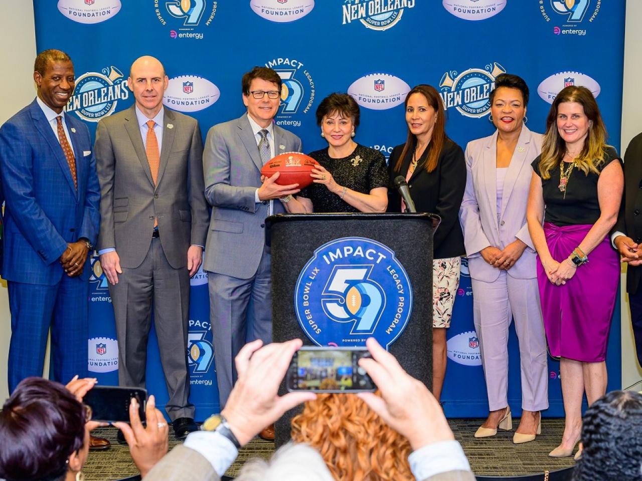 People on a stage behind a podium holding a football