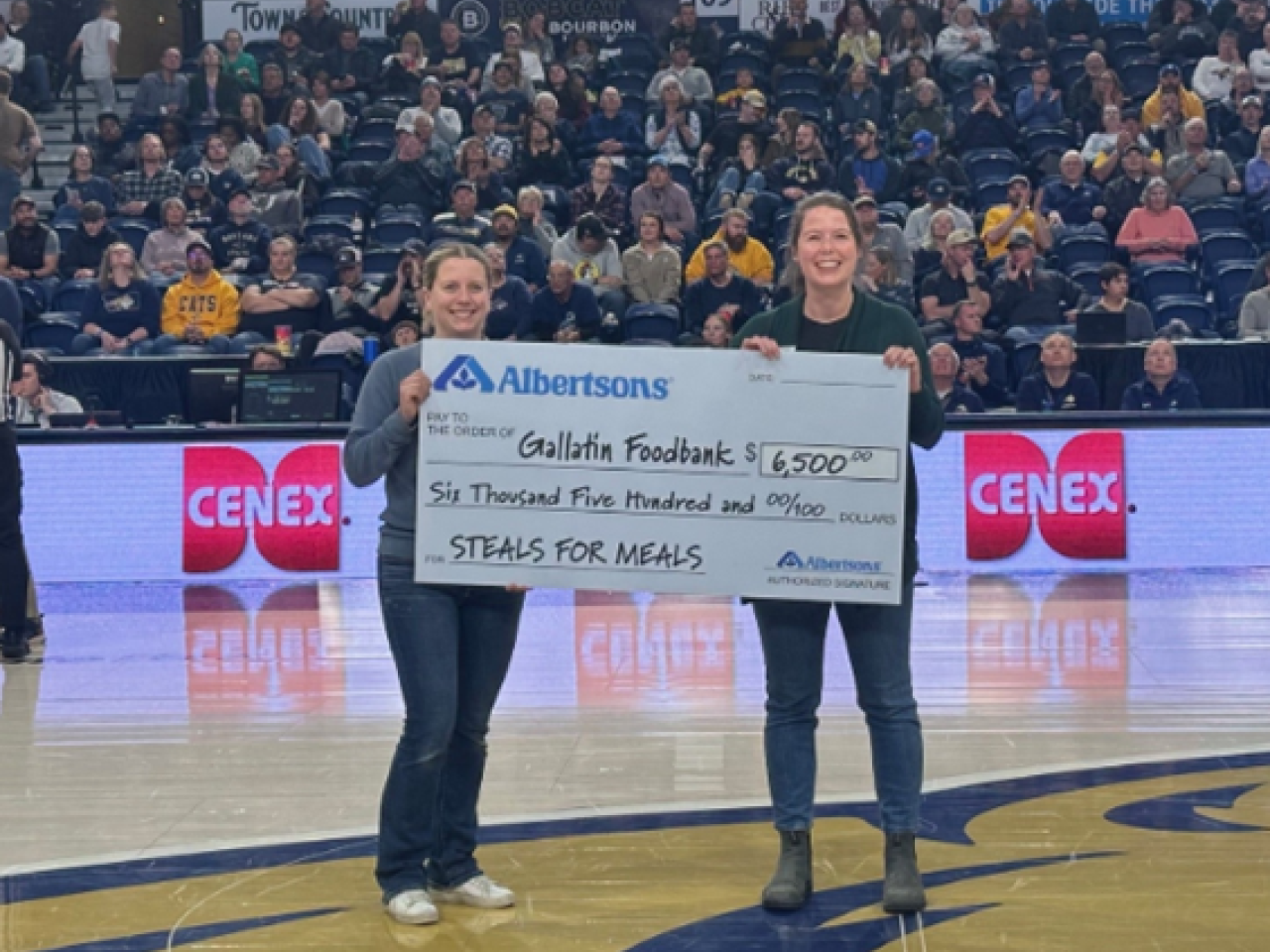 Two people holding a check on a basketball court