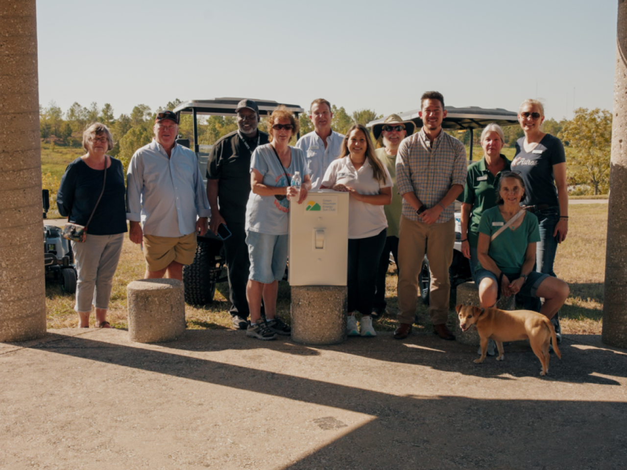 Group of people and a dog stand around in sunny area with oversized prop light switch.