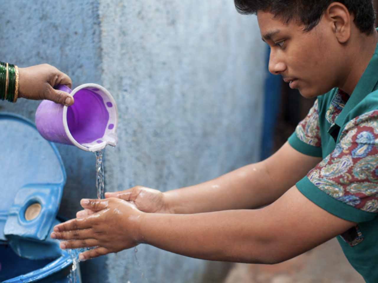 Young person having water poured over his hands so that they can wash them.