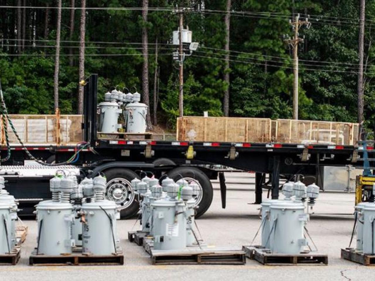 A semi truck in a parking area. Electrical equipment and a person in a forklift in front of it.