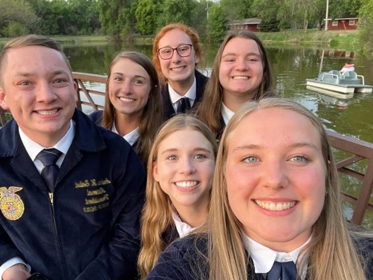 Kids posed in a group selfie on a pier over a small body of water.