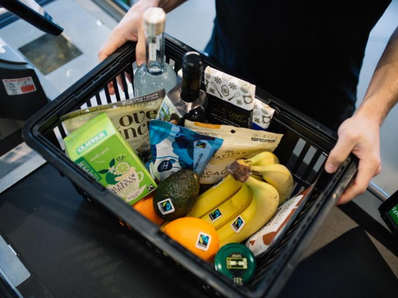 A basket of grocery items with the Fairtrade Mark, including oranges, bananas, tea, avocado, cocoa powder, and more. 