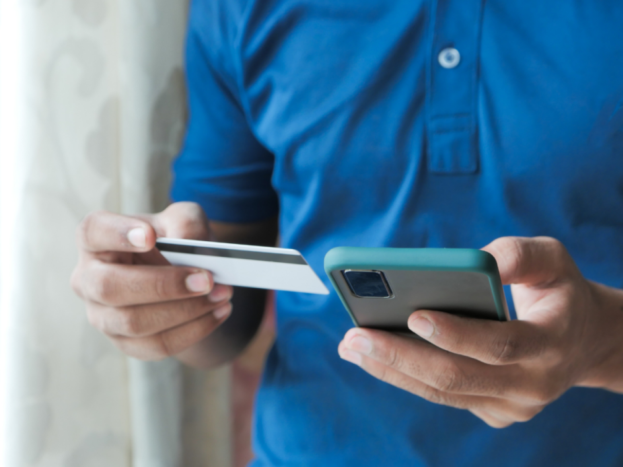 A person holding a credit card in one hand and using a cell phone with the other.