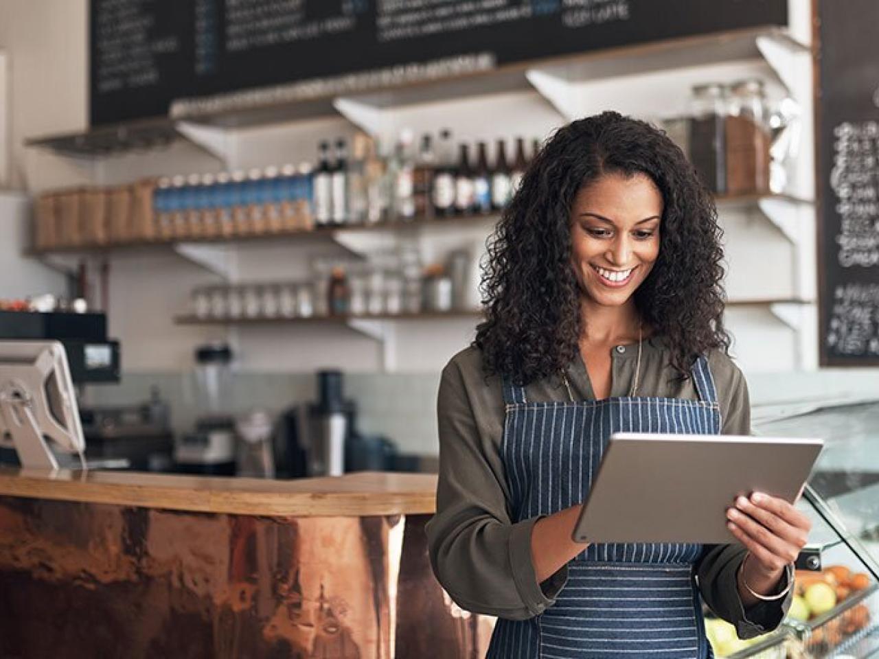 A smiling person works on a tablet device in a cafe setting.