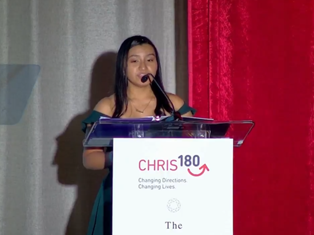 A person speaking at a podium. "CHRIS 180" sign in front.