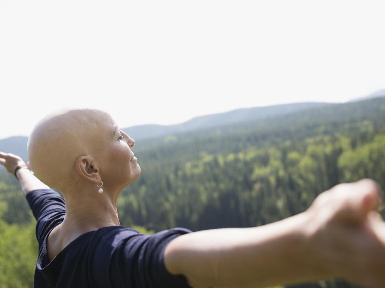 Female cancer patient shown in a field with her arms raised.