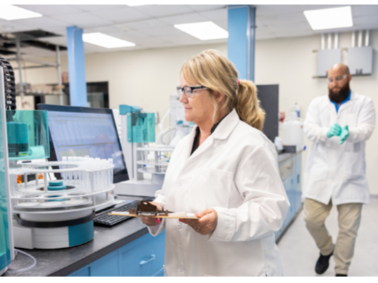 People working in a lab setting, wearing protective clothing.