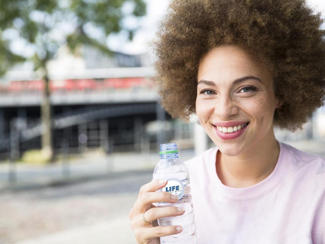 A smiling person holding a plastic bottle outside.