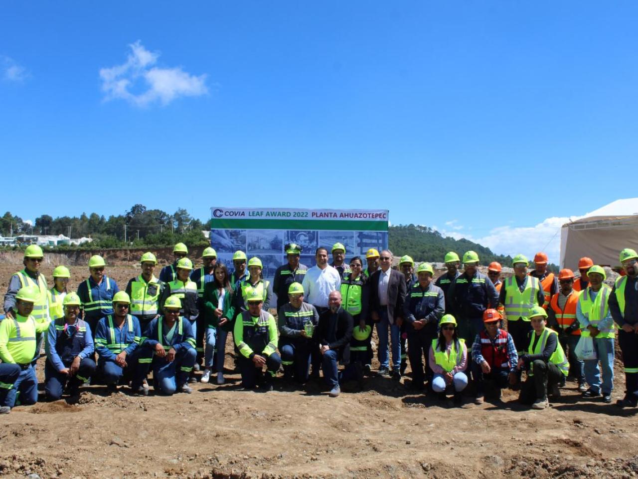 A large group posed outside. Each in high-vis vest and hard hats.