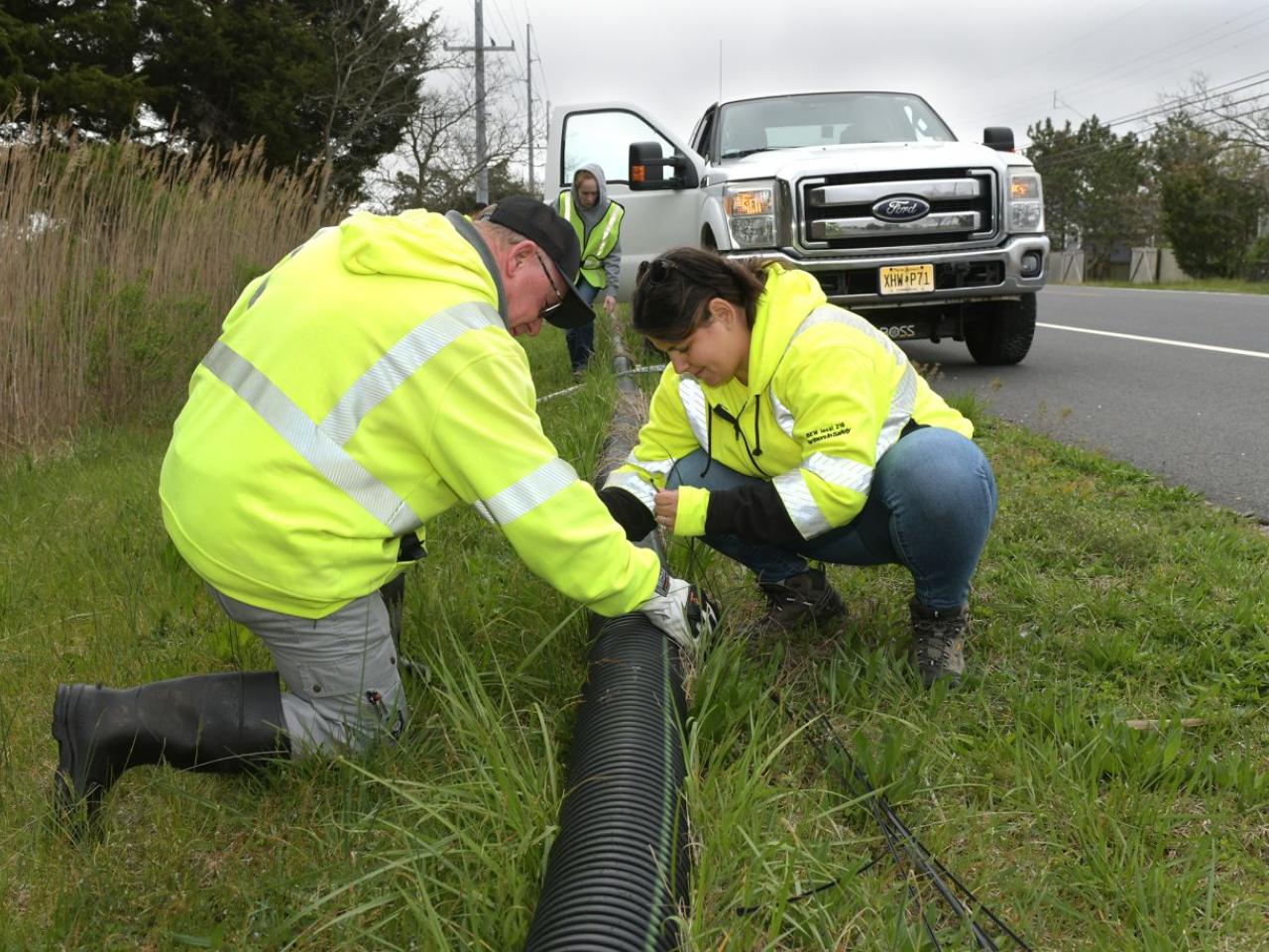 Volunteers working with a drain pipe on the side of a road.