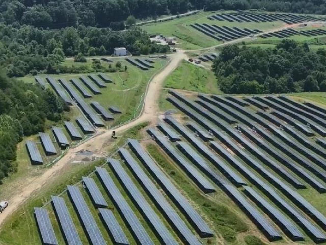 Aerial view of fields of rows of solar panels in a forested area.