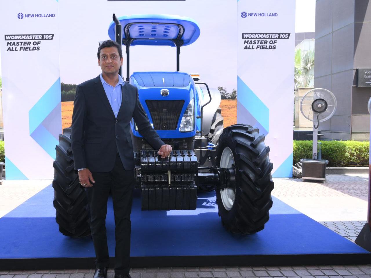 A person standing next to a blue tractor on display.