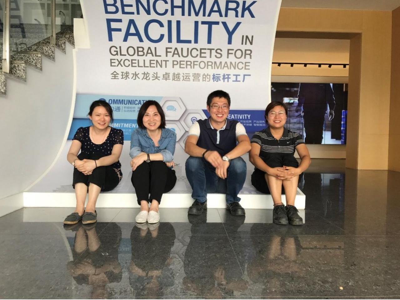 Four people seated in front of a sign "Benchmark facility in global faucets for excellent performance."