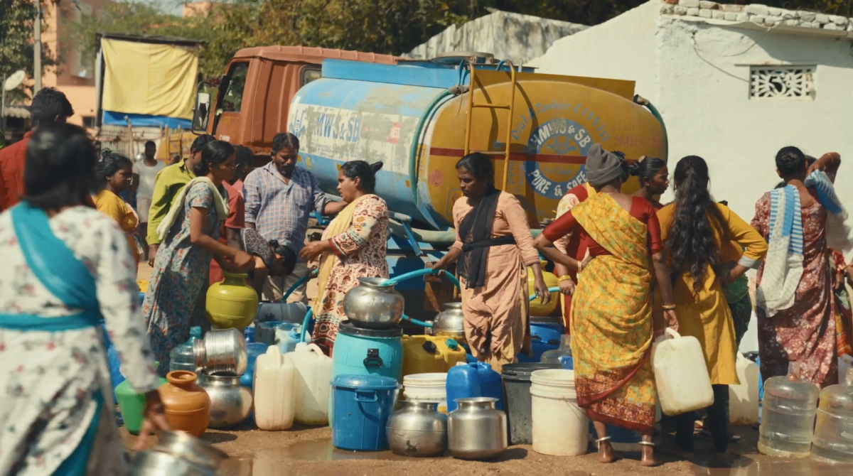 A group of people collecting water from a truck with a water tank.
