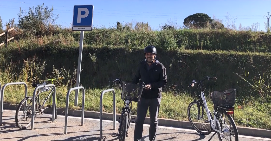 A smiling person standing by a bicycle in a bike parking area.