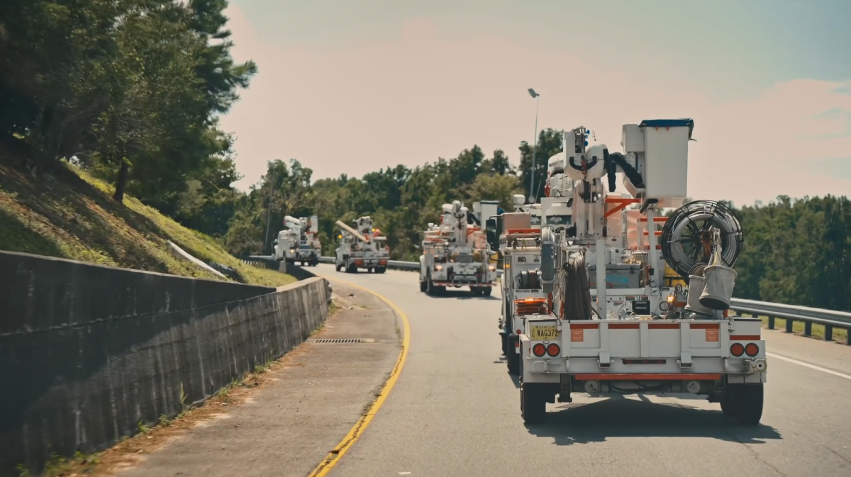 Four line-worker bucket-trucks driving down a road.