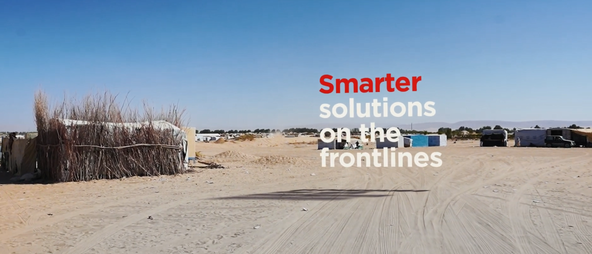 "Smarter solutions on the frontlines" over a sandy area with small buildings in the distance.