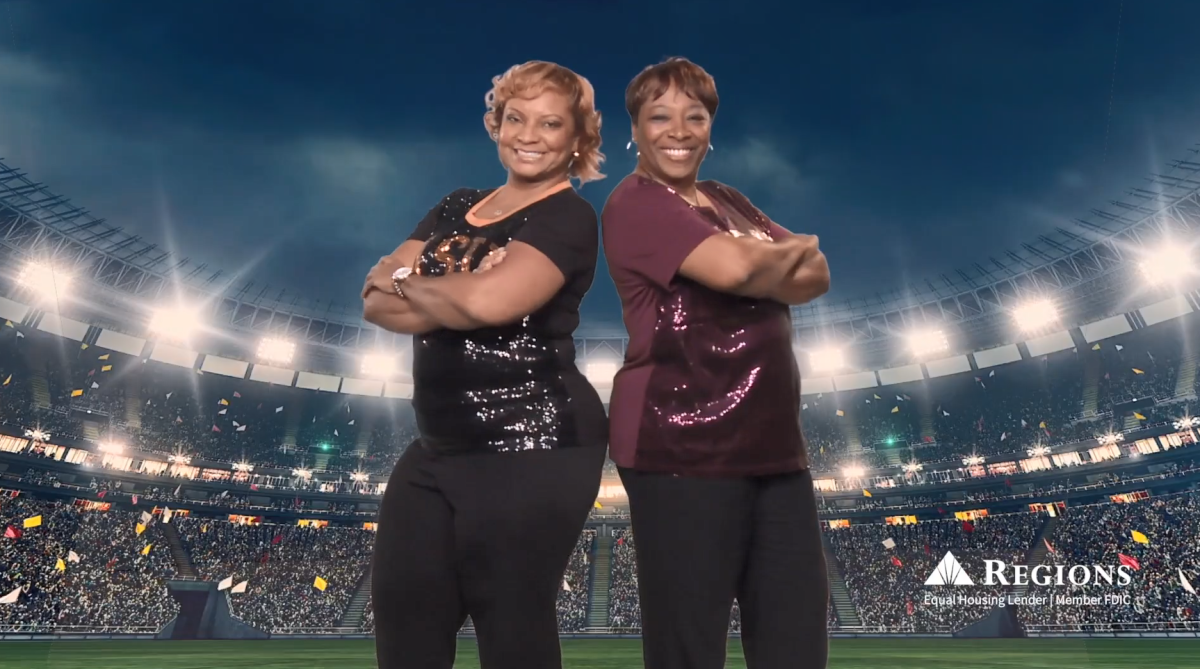 Two smiling people, leaning back to back with arms crossed. A stadium backdrop behind them.