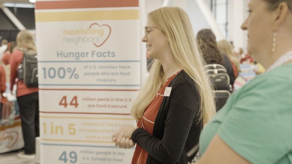 Two people talking in front of Nourishing Neighbors sign with hunger facts