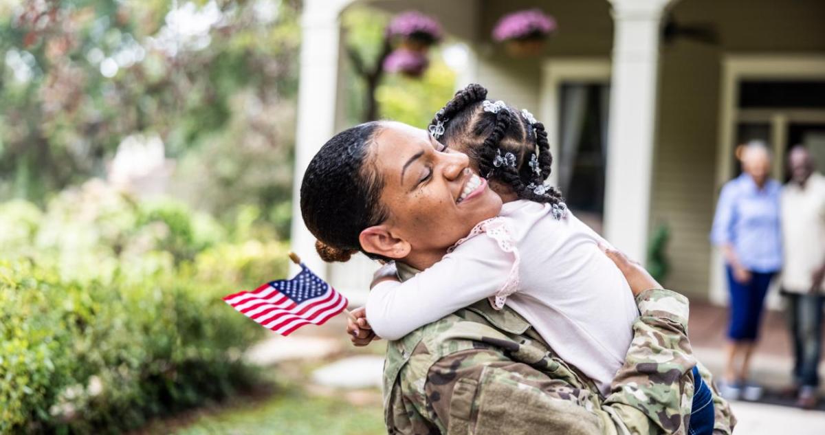 A veteran hugging a young child who is holding a small American flag