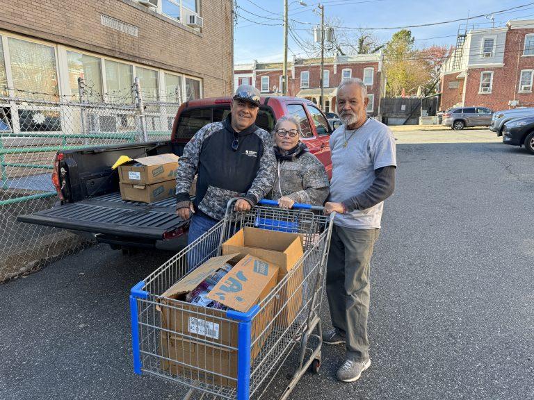 Three people pushing a grocery cart with boxes in it