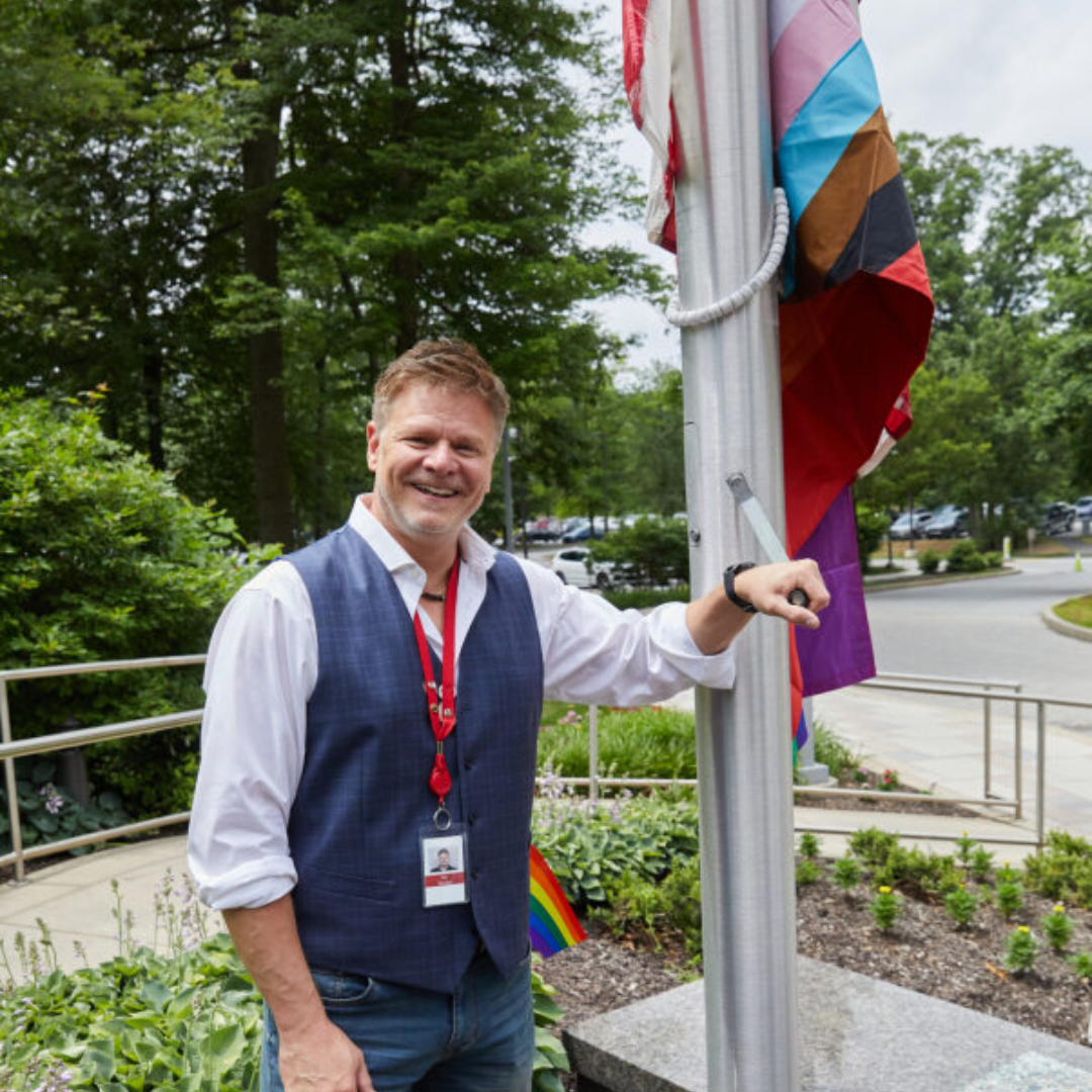 Man standing with hand positioned to raise the Pride Flag at QVC's Studio Park