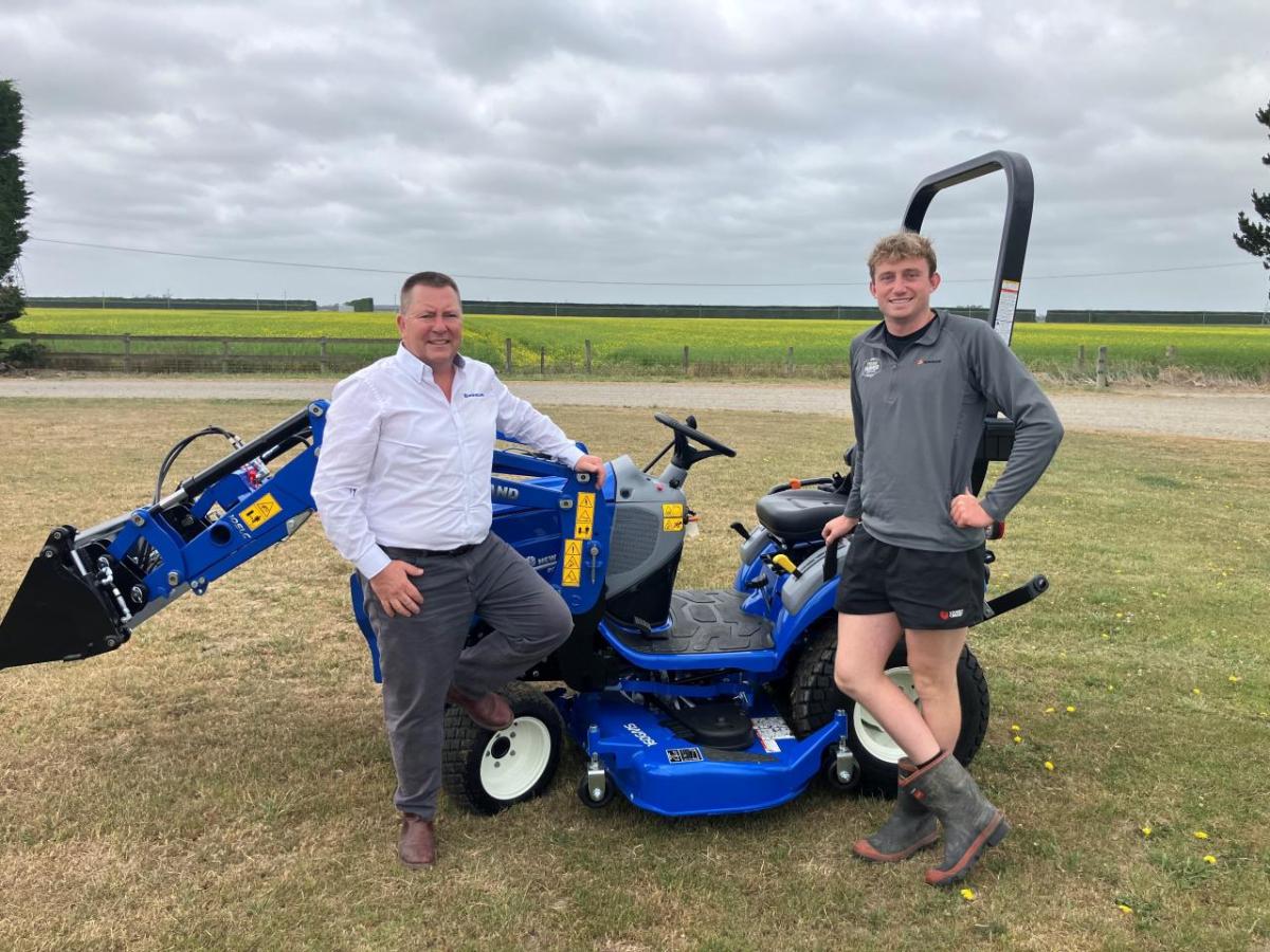 Two people standing in a field next to a blue tractor