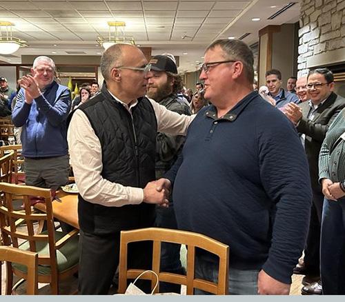 Two people shaking hands in front of people applauding