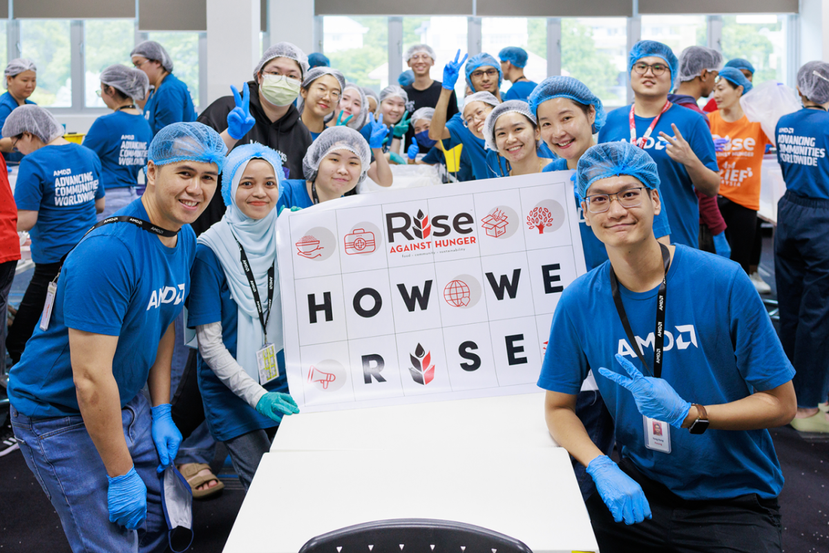 People in AMD t-shirts, gloves and hair nets posing for the camera with a sign that says: "How We Rise"